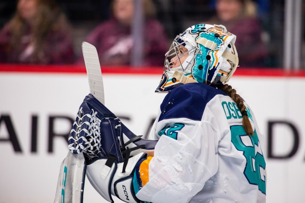 Osborne kneels and looks up at something out of frame. She is wearing a white away uniform.