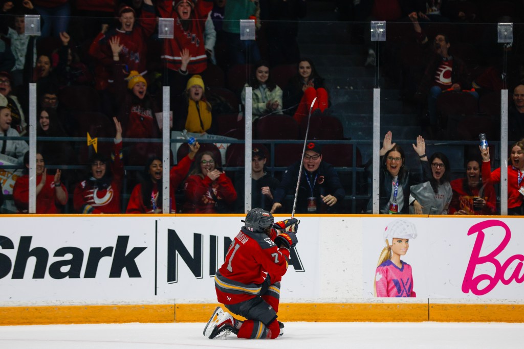 Kadriova pumps her fists as she drops to her knees and points to the crowd in celebration. She is wearing a red home uniform.