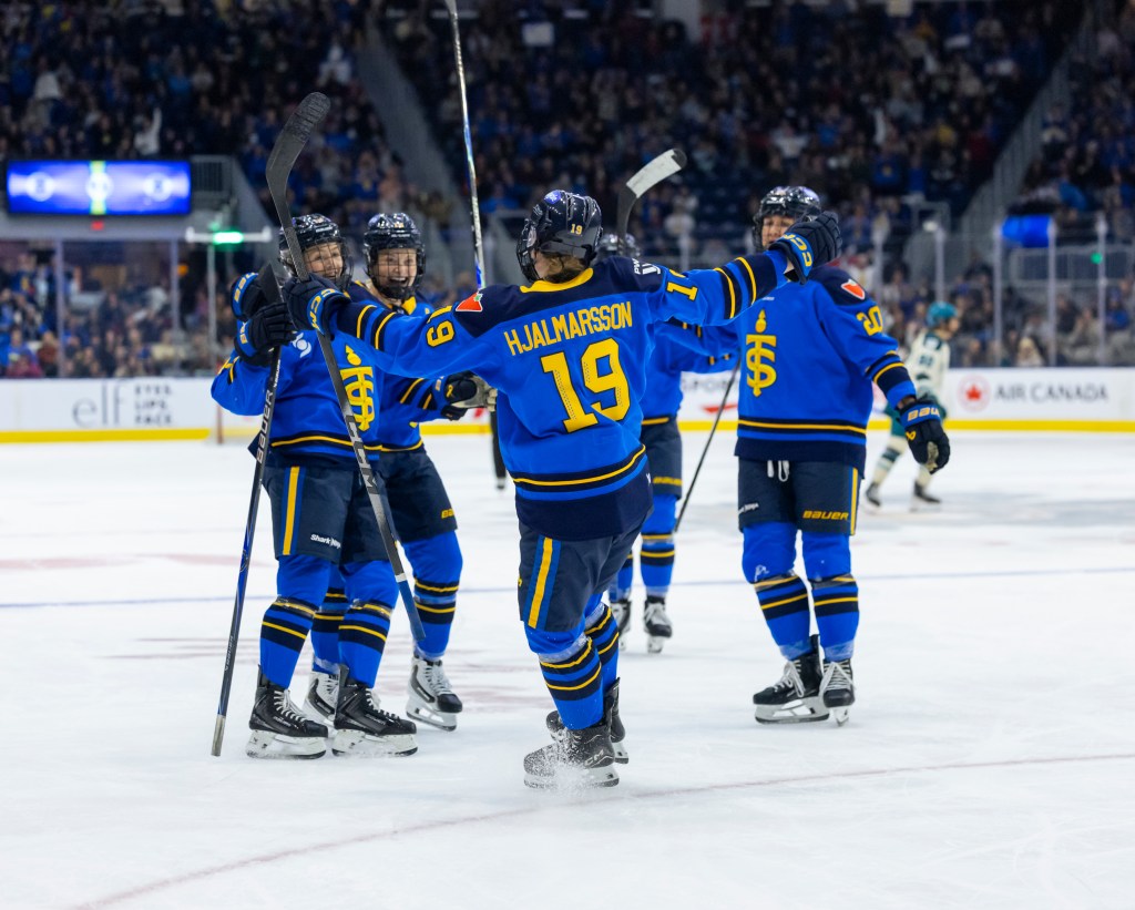 Five Sceptres players smile and celebrate a goal with a group hug. They are wearing blue home uniforms.