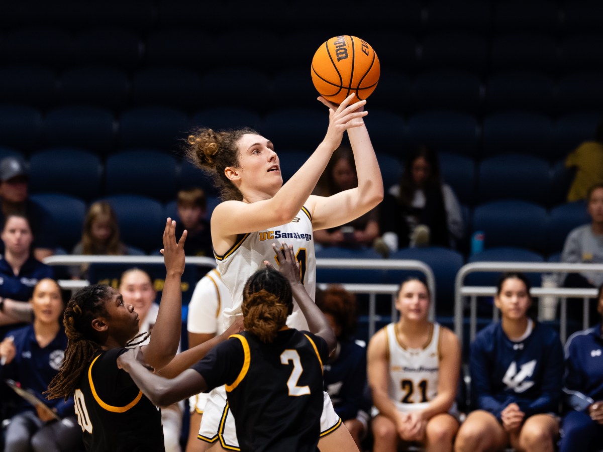 UC San Diego forward Erin Condron goes up for a shot with multiple Long Beach State defenders around her. Her teammates watch from the bench in the background.