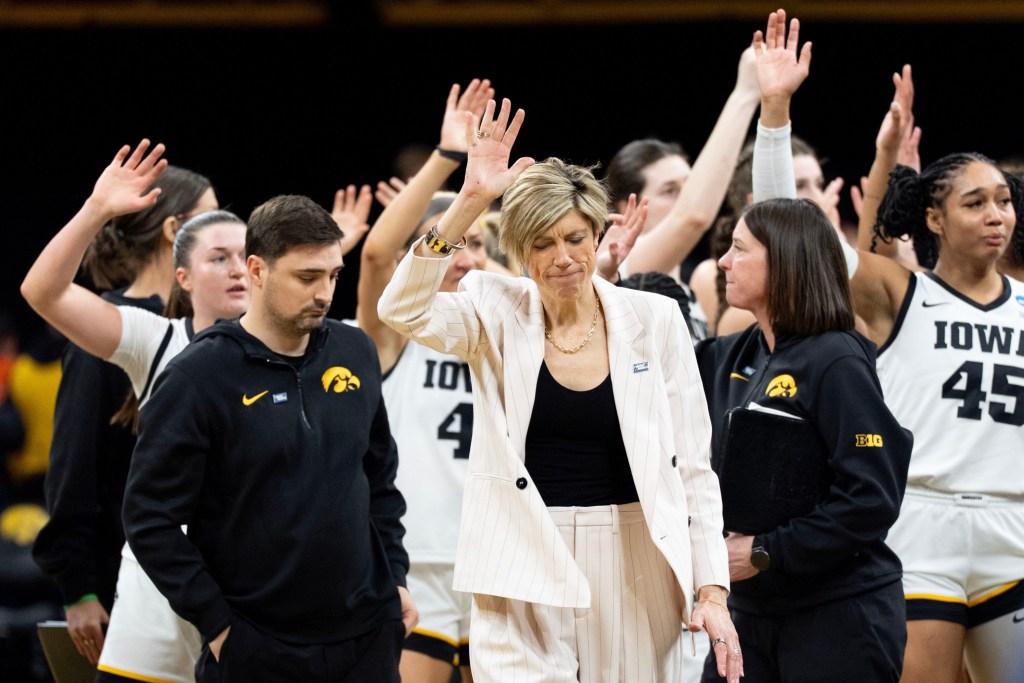 Iowa head coach Jan Jensen, with her head down, Hawkeyes women’s basketball team and staff wave to fans as they walk off the court following a double overtime loss to against the Virginia Cavaliers.