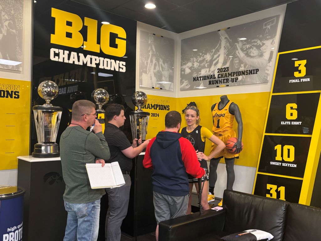 Iowa guard Kylie Feuerbach stands in front of a display showing Iowa's history of Final Four and Big Ten success and speaks with a small group of reporters.