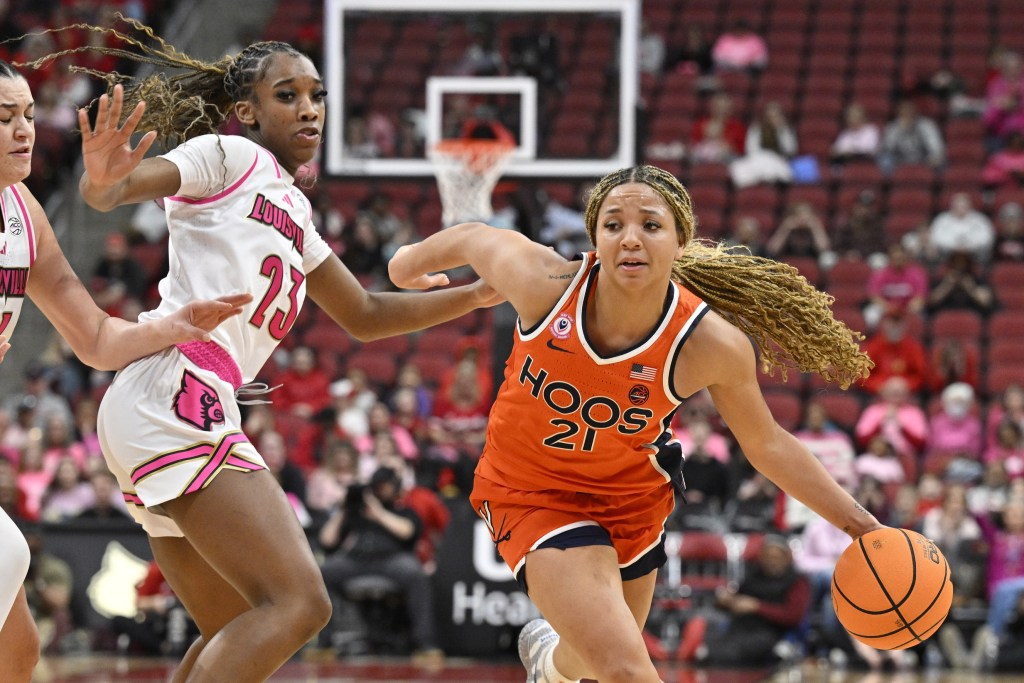 Virginia guard Kymora Johnson dribbles the ball with her left hand. Two Louisville defenders try to slow her down, but neither appears to be in position to cut off her driving lane.