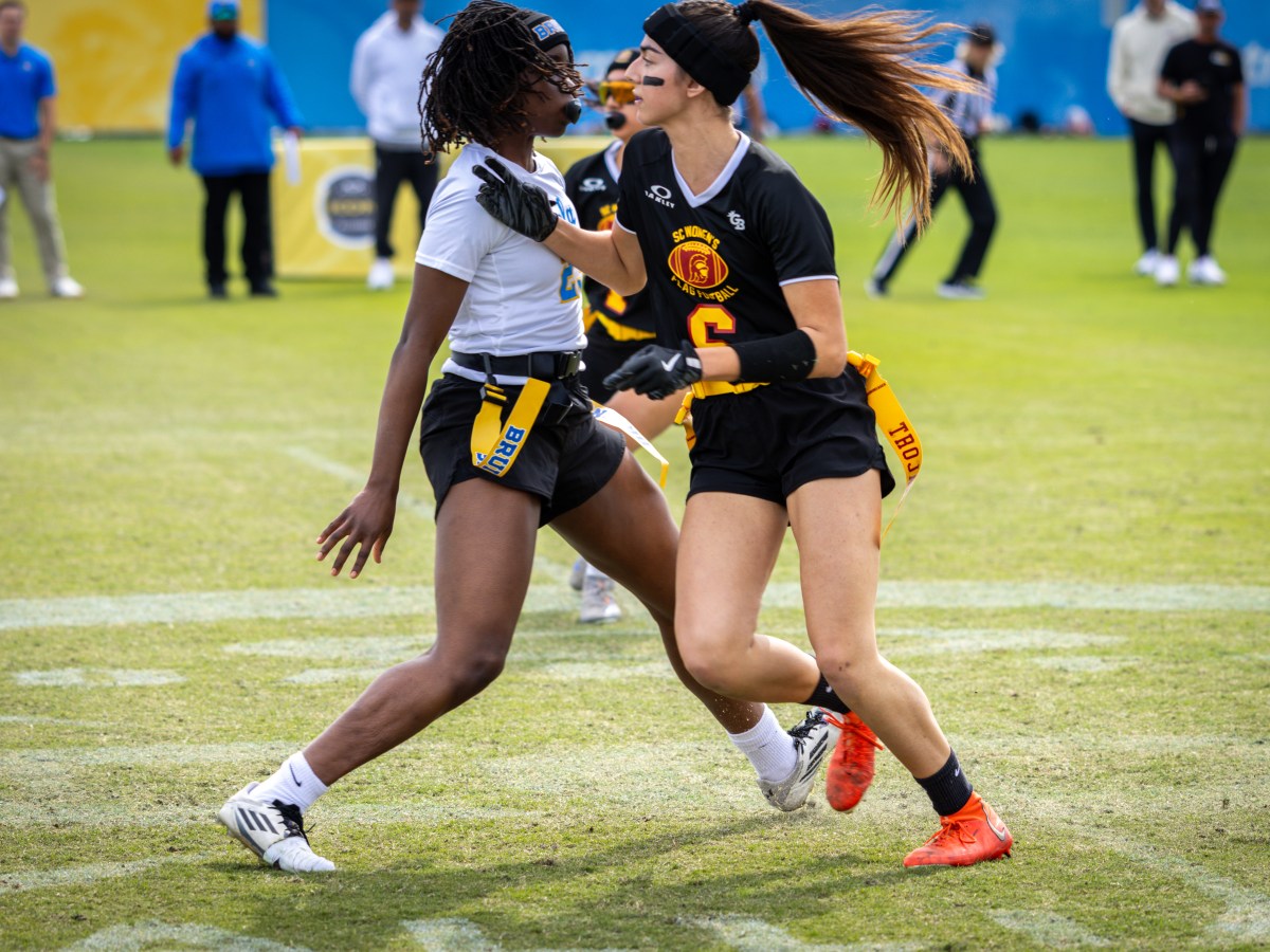 USC flag football player Alia Pasternak (6) runs past a UCLA defender on her right side while coaches and referees watch from the sideline.