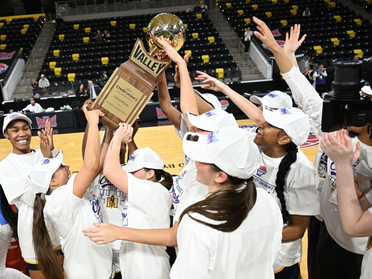 Murray State players lift up the championship trophy after winning their second straight MVC Tournament at XTream Arena in Coralville, Iowa, on March 15, 2026. The players are all wearing white championship t-shirts and hats.
