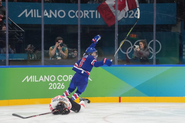 Keller raises her arms in celebration after scoring the gold-medal-clinching goal, while Thompson looks devastated on the ice. Keller is wearing a blue home uniform, while Thompson is in a white away one.