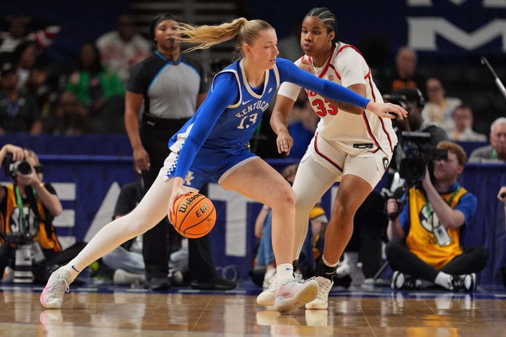A player in a blue uniform and a blonde ponytail carries the basketball down the court.