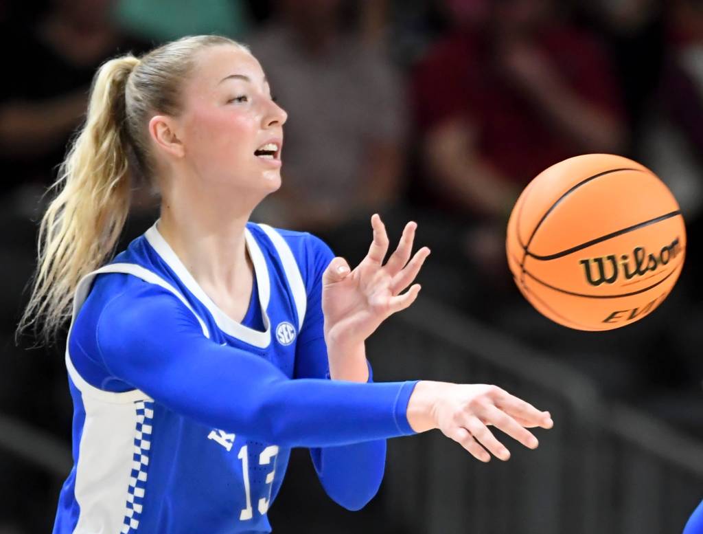 A player in a blue long-sleeved uniform and a blonde ponytail tosses the basketball.