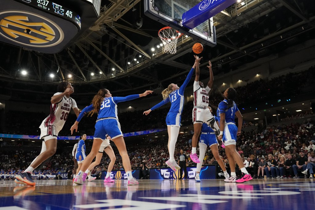 Players in blue and white uniforms jump for the ball on a basketball court 