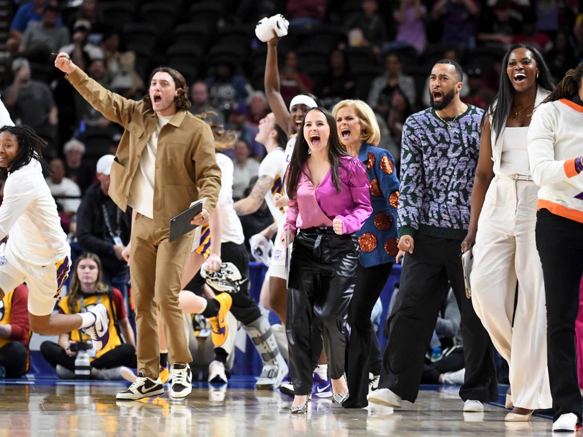 Members of the LSU team, with some dressed in the team's white uniform and coaches dressed in various attire, leap onto the court to celebrate a play.