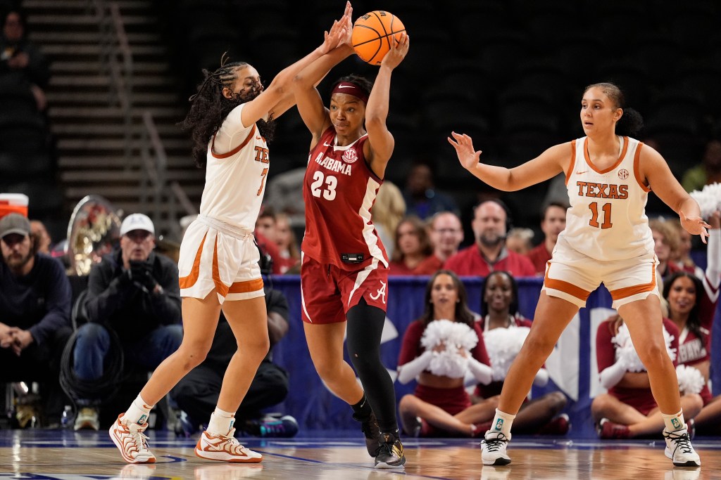 A defender for Texas, wearing white, thwarts a player for Alabama, wearing red, who has the basketball.