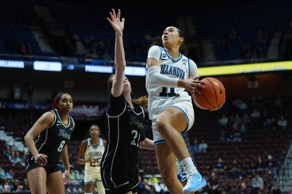 Villanove guard Jasmine Basco in a white jersey elevates past a Providence defender in a black jersey as Basco is in the early stages of a scoop layup to her left