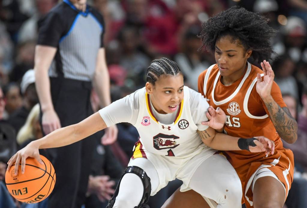 Two players battle for a basketball. One wears a white uniform and the other wears an orange uniform. 