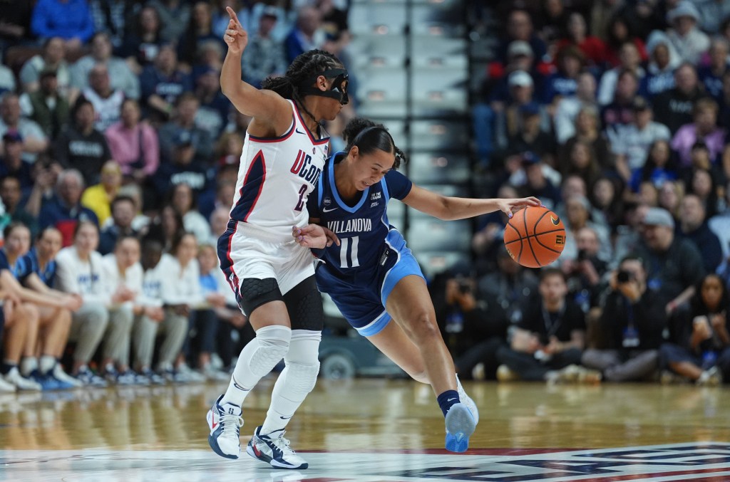 Two players battle for the ball on the court. The player on the left wears a white jersey and the player on the left wears a blue jersey. 