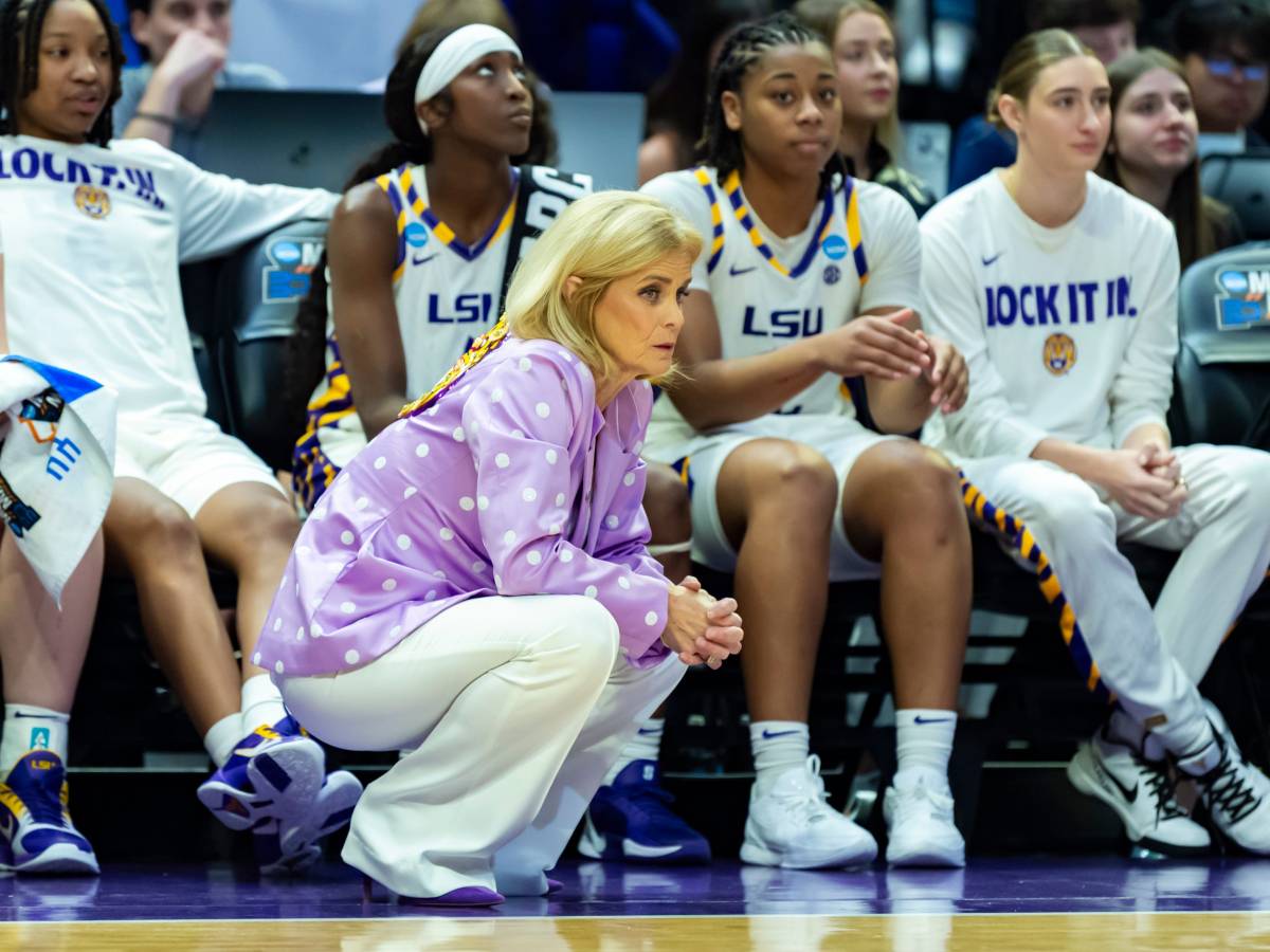 Kim Mulkey knees on the sideline in front of her team's bench
