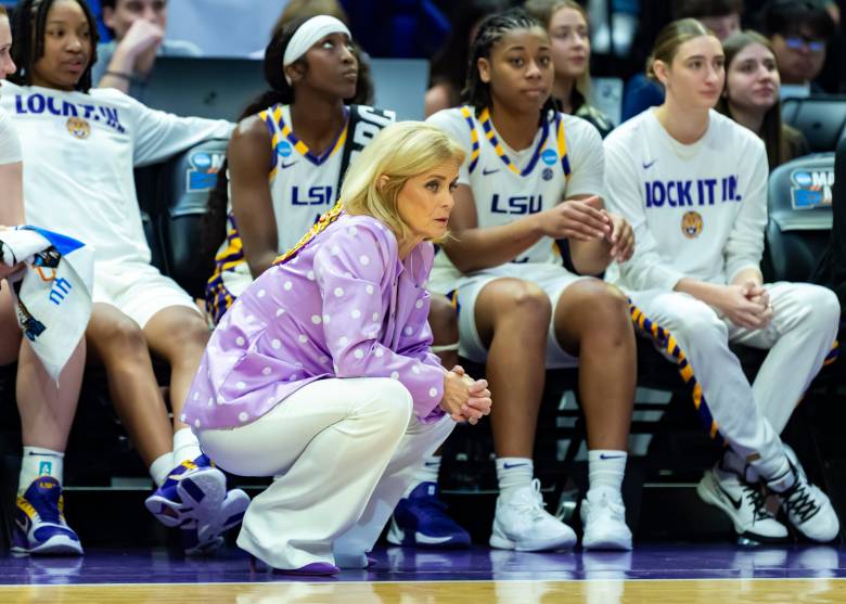 Kim Mulkey knees on the sideline in front of her team's bench