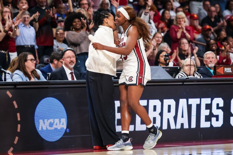 South Caroliona Raven Johnson and head coach Dawn Staley hug on the sideline. There is a large crowd behind them.