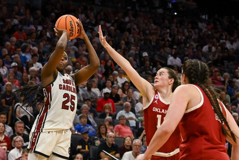 South Carolina guard Raven Johnson shoots the ball over an Oklahoma defender. The ball is still in her hands and two Oklahoma defenders are standing next to her.