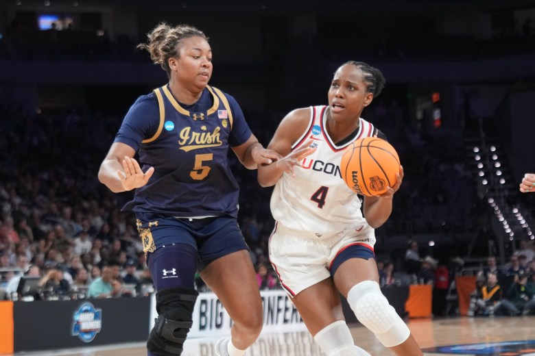 Two players battle for a basketball on the court. One wears a blue jersey and the other wears a white jersey.
