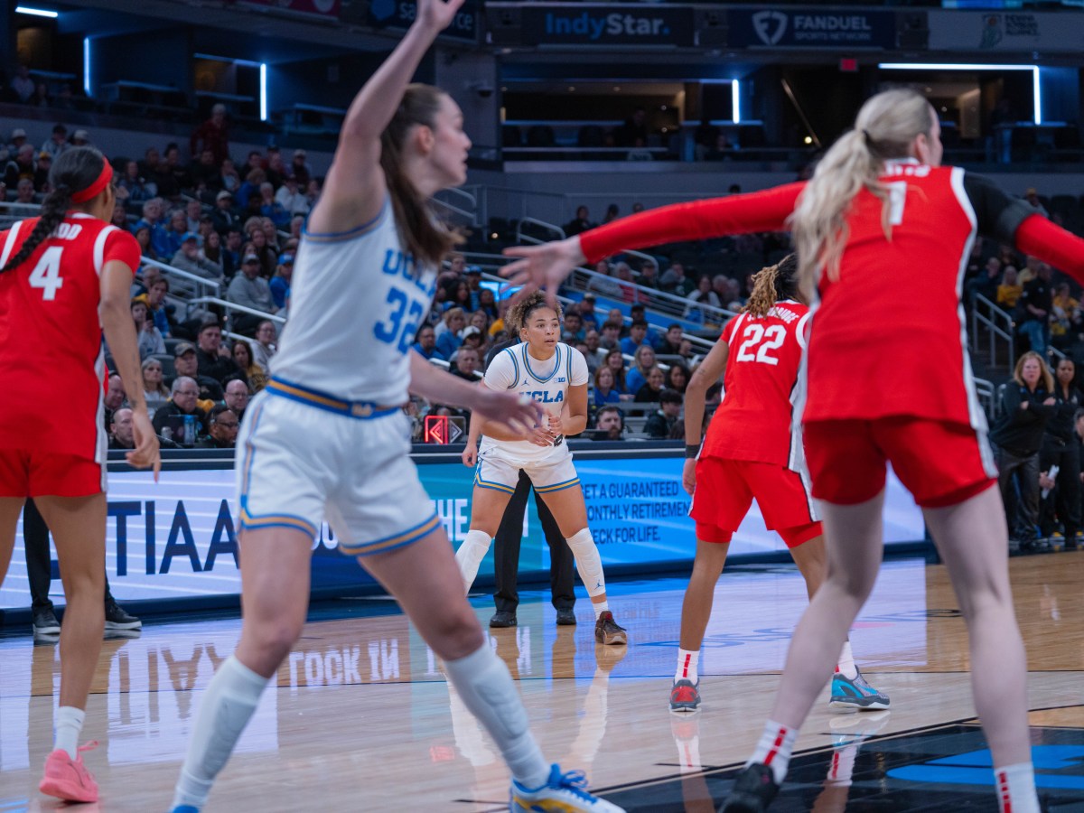 Guard Kiki Rice wearing white jersey with blue trim, standing in the background. In the foreground are three Ohio State players wearing scarlet jerseys and one UCLA player wearing a white jersey with blue trim.