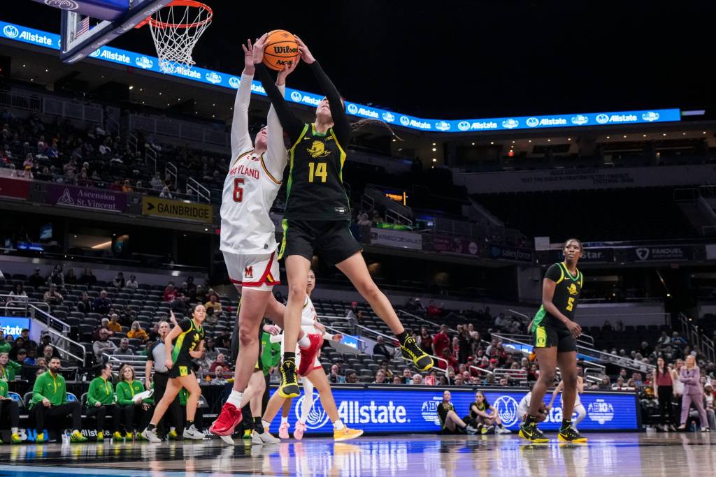 Marylan guard Saylor Poffenbarger and Oregon guard Ari Long are depicted in midair with their arms outstretched, each with both their hands on a ball coming down off the net in an attempt to secure a rebound.