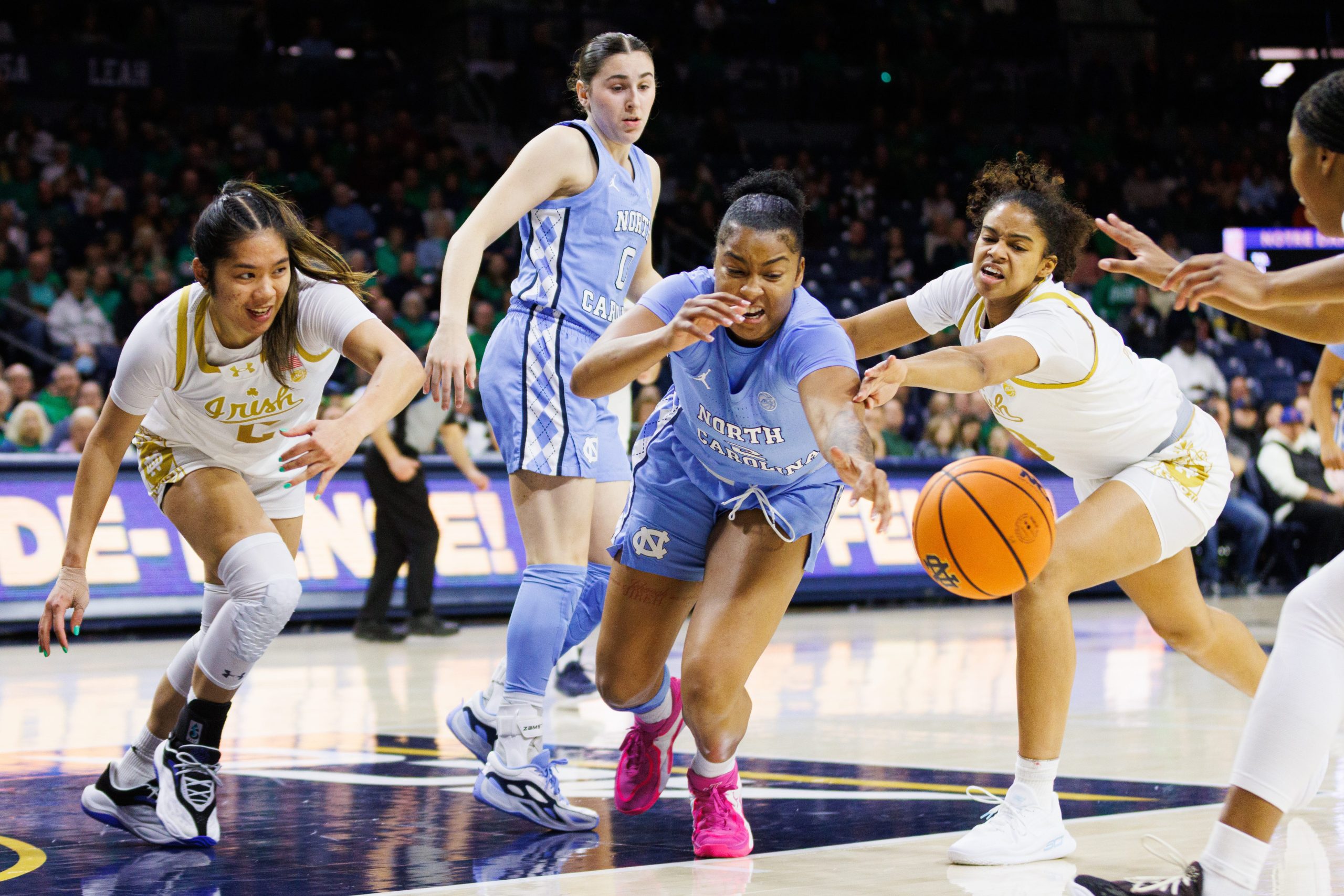 North Carolina forward Nyla Harris dives for a loose ball near the net, with her left arm outstretched. Several Notre Dame players are diving with her.