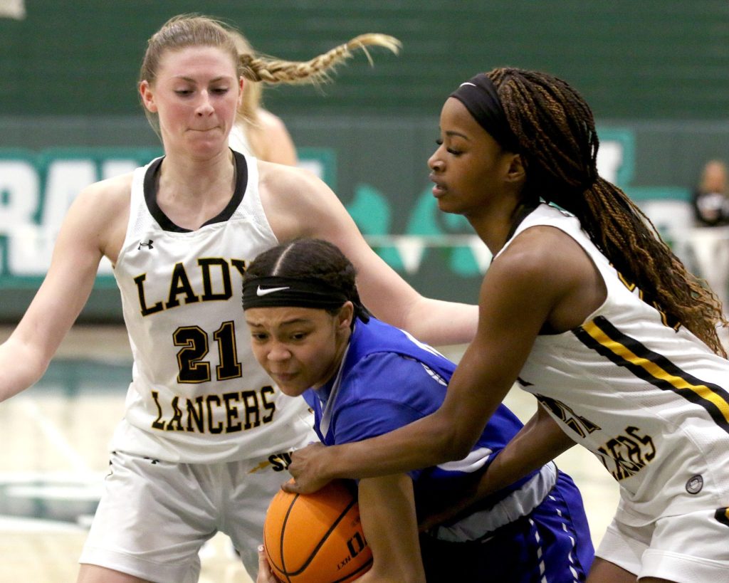 Paul VI guard Hannah Hidalgo holds the ball with both hands near her right hip, bending down to try to shield it from defenders. St. John Vianney guard Madison St. Rose reaches in to grab it, and a St. John Vianney teammate also pressures Hidalgo from the other side.