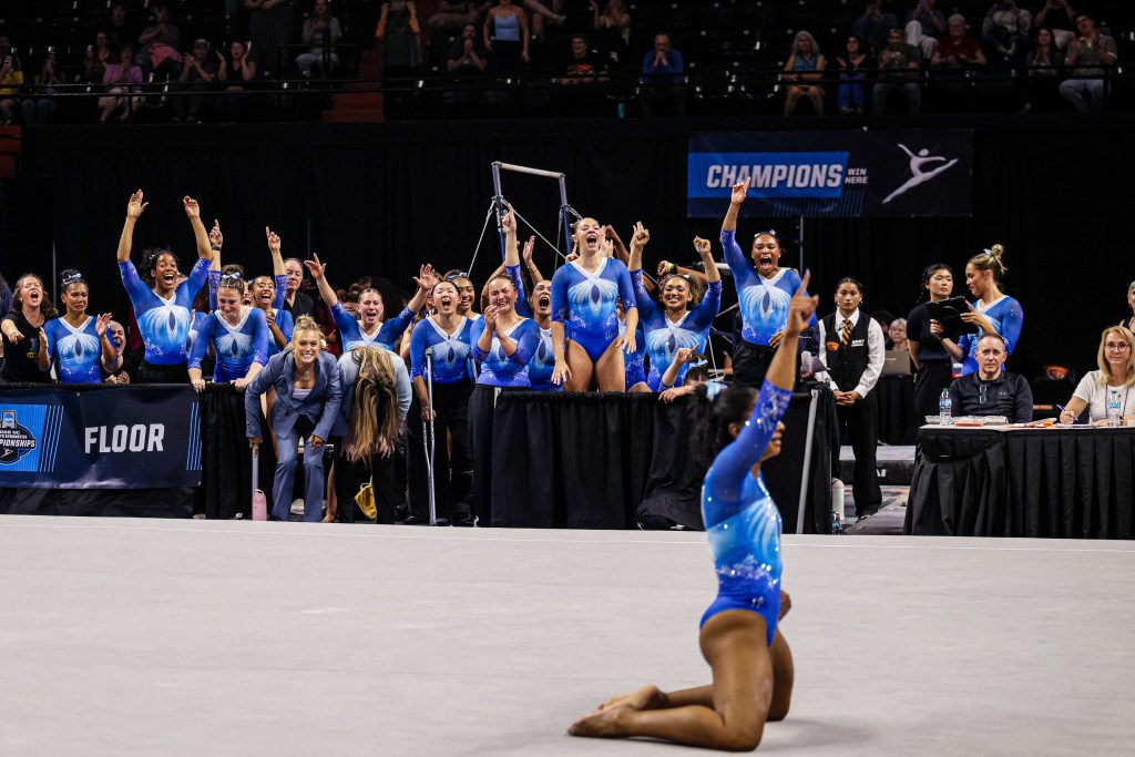 Jordan Chiles completes a floor routine in a blue leotard, with her teammates cheering in the background