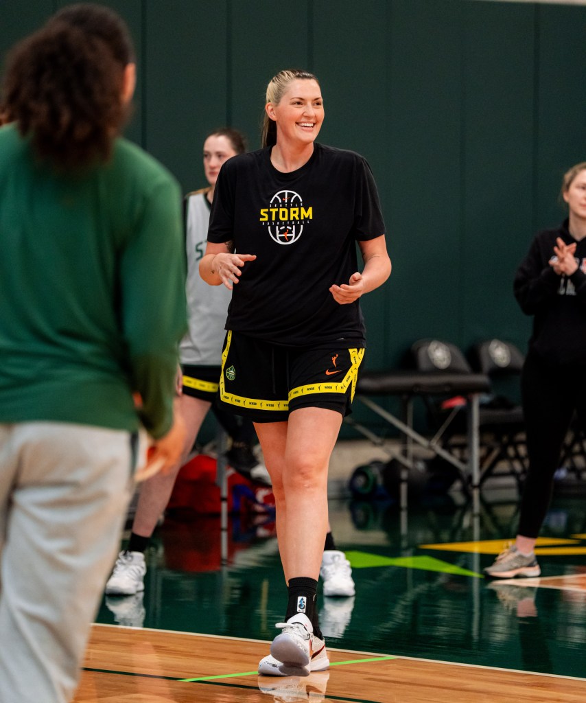 Stefanie Dolson smiles and holds her arms at a 90 degree angle as she walks onto the court at training camp.