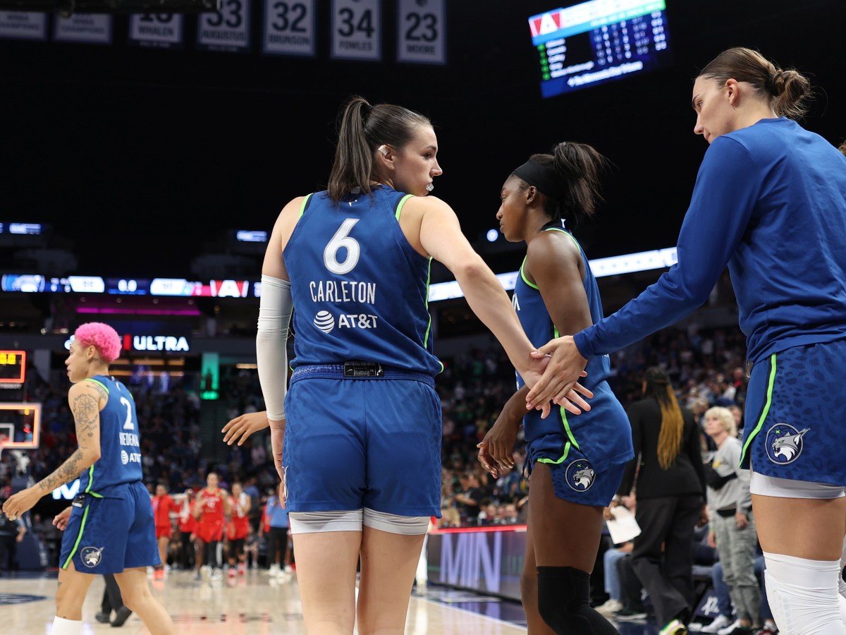 Bridget Carleton in her blue uniform, looks back and greets Maria Kliundikova. Natisha Hiedeman is in the background with her pink hair.