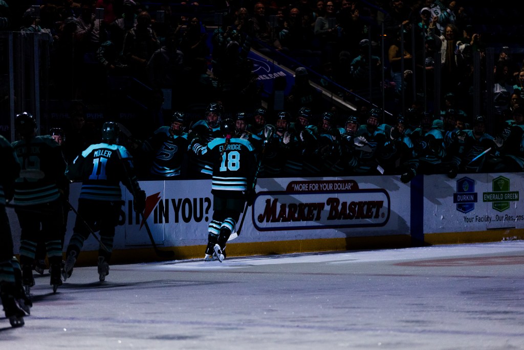 Eldridge skates down the handshake line with Müller trailing her. They are wearing green home uniforms.