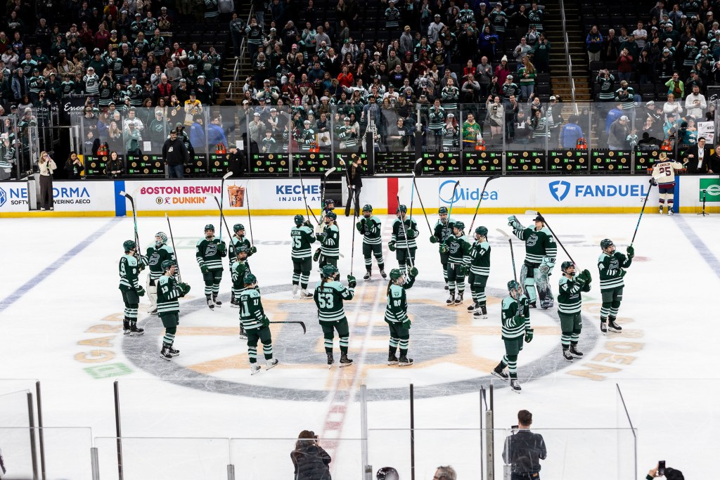 Fleet players stand around the center ice circle and raise their sticks in salute of the crowd. They are wearing green home uniforms.