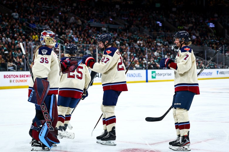 Victoire players celebrate by fist-bumping Ann-Renée Desbiens. They are wearing cream away uniforms.