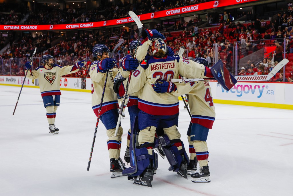 Abstreiter's teammate surround and hug her. They are all wearing cream away uniforms.