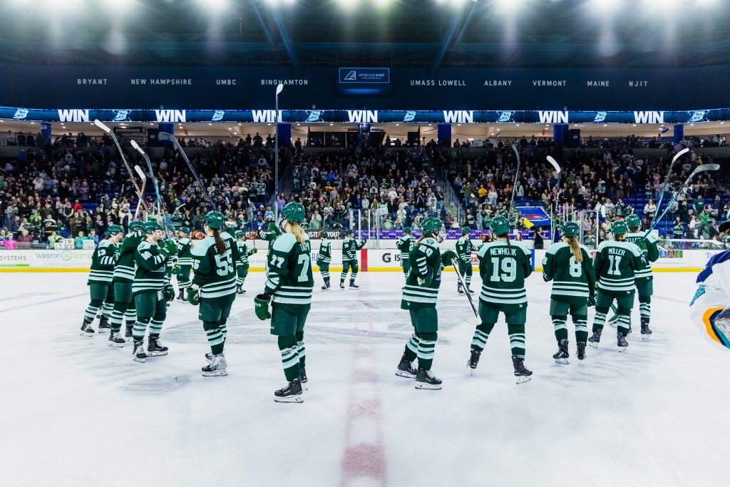 The Fleet stand around the center ice circle and raise their sticks in salute of the crowd. They are wearing green home uniforms.