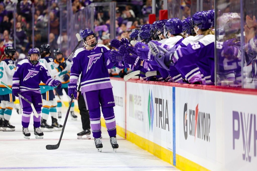Stecklein leads the handshake line down the bench after scoring. She and her teammates are all wearing purple home uniforms.