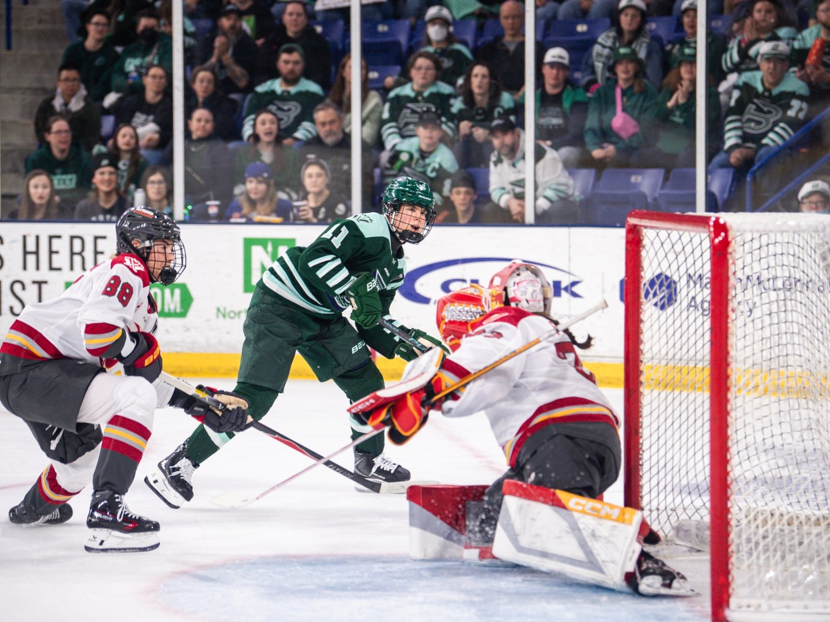 Müller smiles as she sees the puck get past a sliding Philips. Müller is wearing a green home uniform, while Philips is in a white away one.