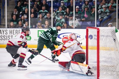 Müller smiles as she sees the puck get past a sliding Philips. Müller is wearing a green home uniform, while Philips is in a white away one.