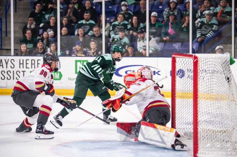 Müller smiles as she sees the puck get past a sliding Philips. Müller is wearing a green home uniform, while Philips is in a white away one.