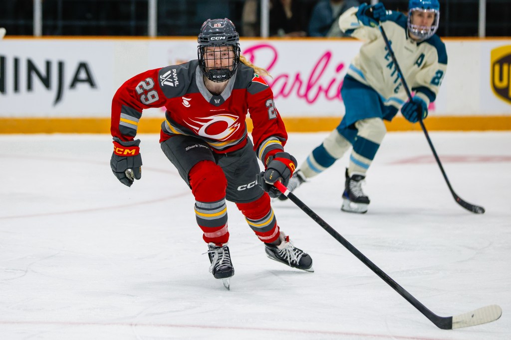 Hemp skates after the play with her stick outstretched. She is wearing a red home uniform.