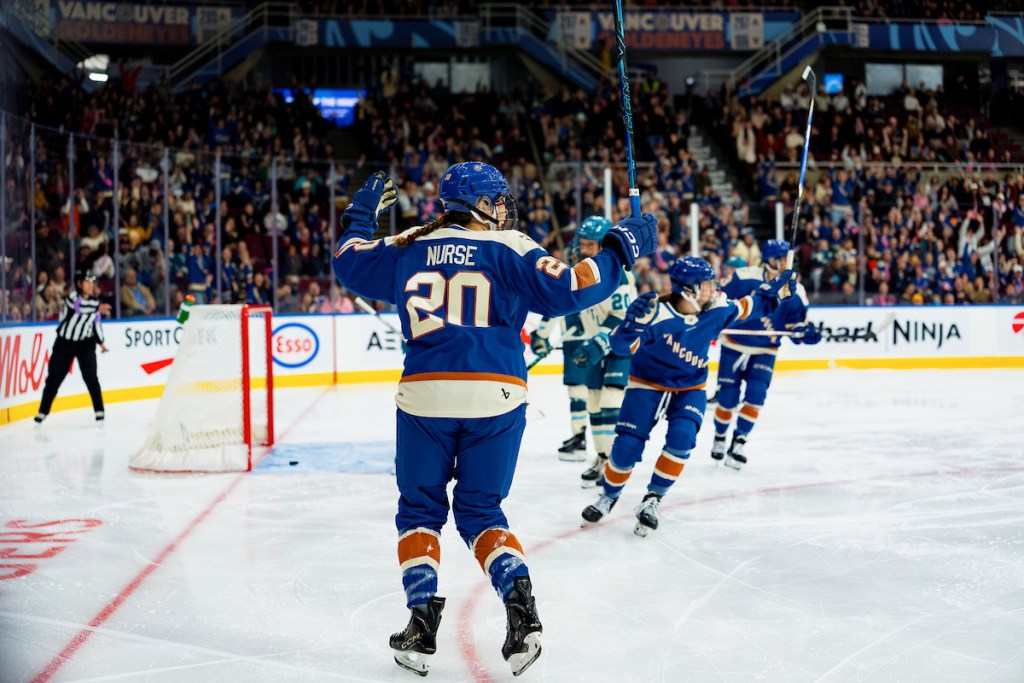 Nurse and her teammates all raise their sticks in celebration and look toward the blue line. They are wearing blue home uniforms.