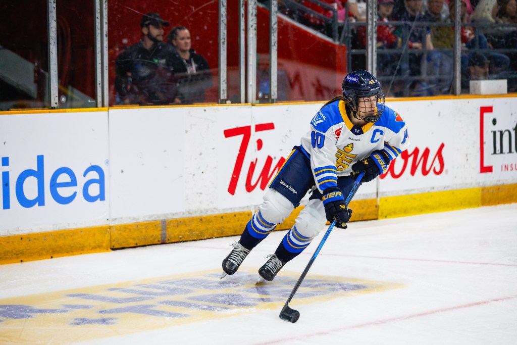 Turnbull looks up ice as she skates with the puck. She is wearing a white away uniform.