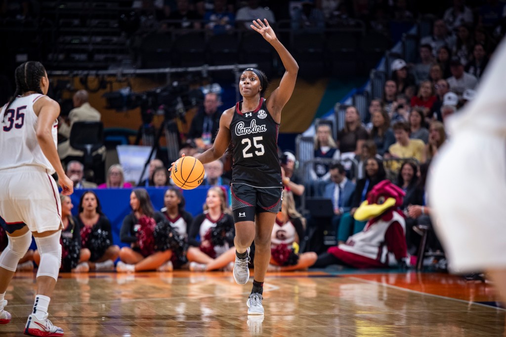 Raven Johnson dribbles the ball with her right hand while holding up four fingers on her left hand to call a play.