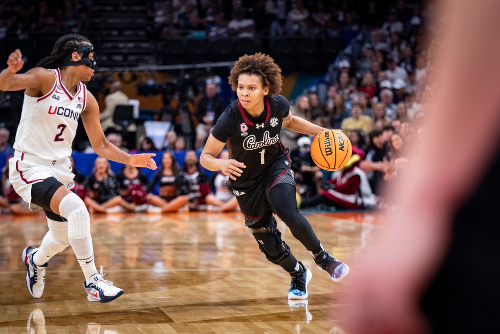 Maddy McDaniel of South Carolina drives past UConn's KK Arnold, who is wearing a black mask, with the ball in her left hand and one foot off the floor.