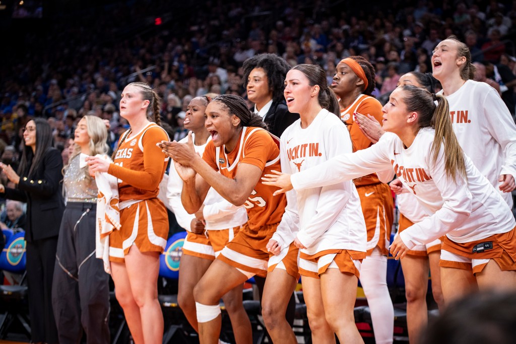 Texas forward Madison Booker cheers and claps her hands from the bench surrounded by teammates on either side.