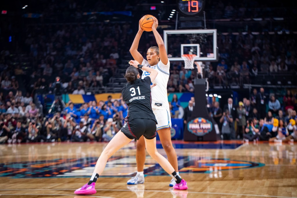 UCLA forward Sienna Betts holds the ball above her head and away from her defender, South Carolina forward Alicia Tournebize.