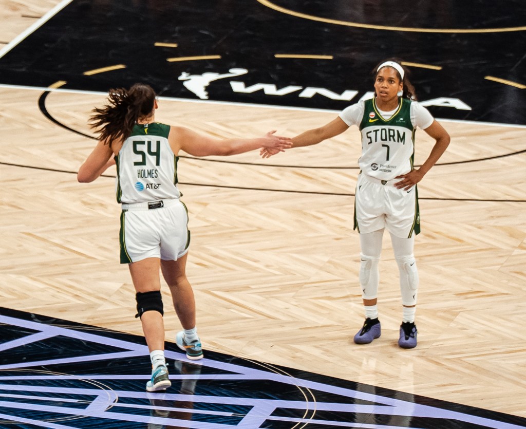 Mackenzie Holmes runs down the court with her back towards the camera and high-fives Zia Cooke as the runs past the guard standing there with her other hand on her hip.