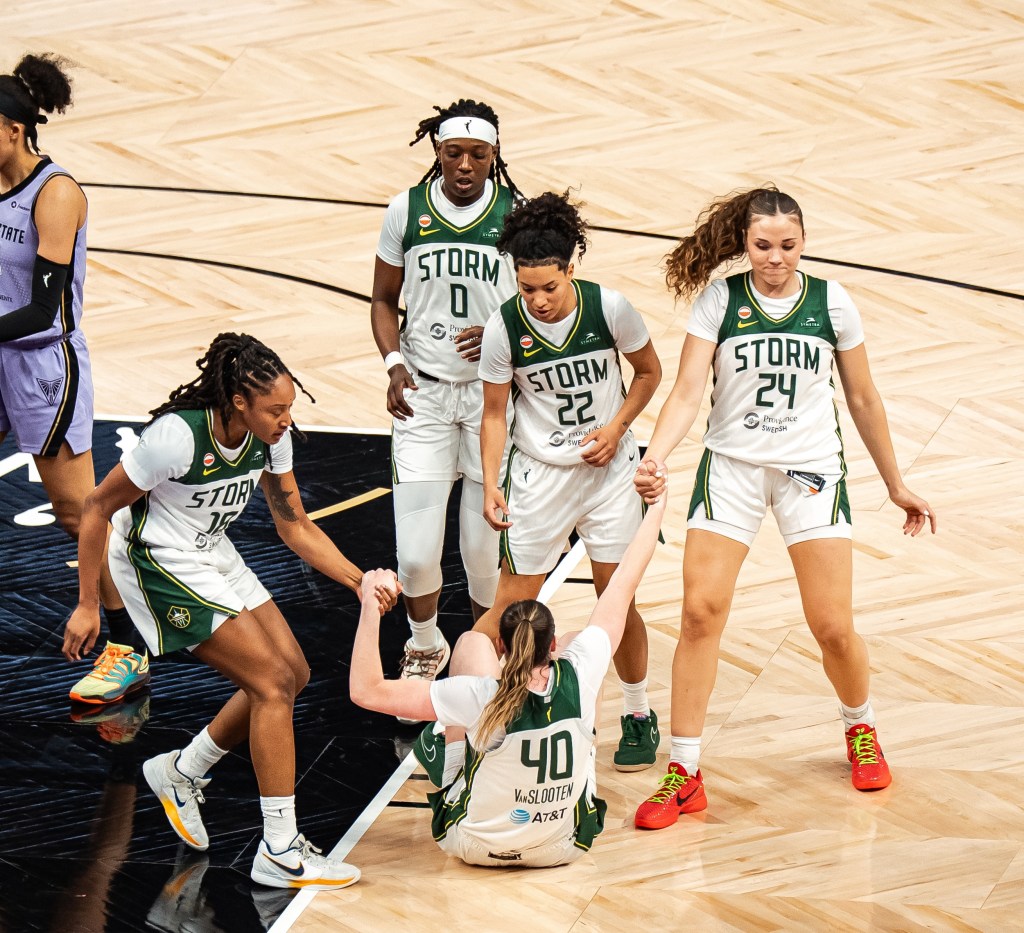 Jaelyn Brown pulls Grace VanSlooten's left arm up while Elle Ladine pulls up her left. Taina Mair and Rennia Davis are nearby between Ladine and Brown, gesturing out as if to also help VanSlooten up.