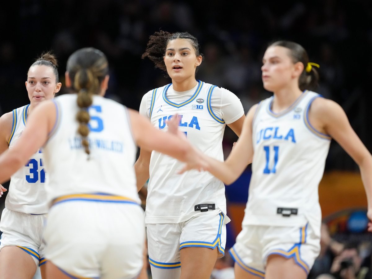 UCLA’s Lauren Betts runs back up court. Teammates Gabriela Jaquez and Charlisse Leger-Walker high-five while crossing her path. The arena is blurred and darkened in the background