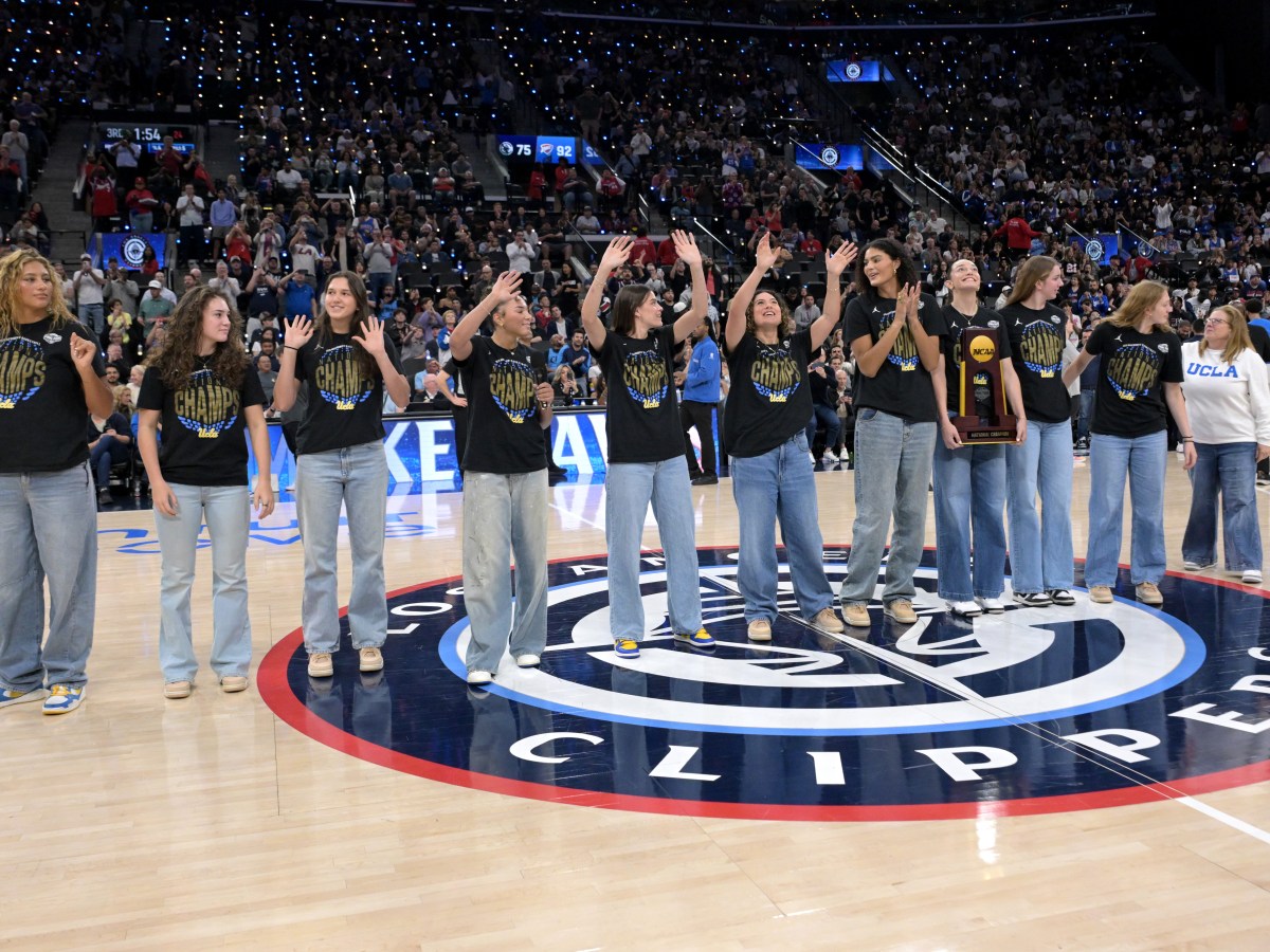The UCLA Bruins wave to the crowd at Intuit Dome while standing in a line at midcourt during a ceremony. The crowd is visible in the seats behind them.